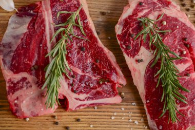 Ahşap kesme tahtasında taze çiğ biftek, siyah arka planda baharatlar, üst manzara..