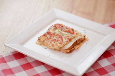 Kare beyaz tabakta küçük bir parça domates lazanyası. Restoranda, kafede ya da lokantada akşam yemeği. Sağlıklı gıda konsepti.