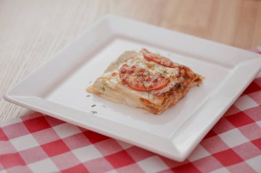 Kare beyaz tabakta küçük bir parça domates lazanyası. Restoranda, kafede ya da lokantada akşam yemeği. Sağlıklı gıda konsepti.