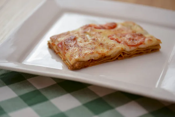 Malý kousek rajčatových lasagní na čtvercové bílé desce. Večeře v restauraci, kavárně nebo bistru. Koncept zdravé stravy. — Stock fotografie