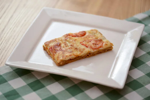 Pequeño trozo de lasaña de tomate en un plato blanco cuadrado. Cena en restaurante, cafetería o cafetería. Concepto de comida saludable . —  Fotos de Stock