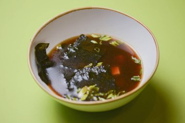 Erişteli Asya ramen çorbası, tofu ve yeşil arka planda Norveç yosunu..