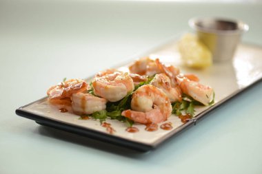 Beyaz bir tabakta servis edilen roka, limon ve maydanoz soslu karides ya da karides salatası.