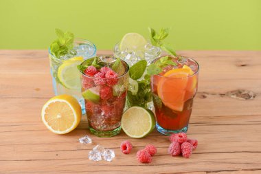 Dört tropikal karışık içki, portakal, limon ve ahududu kokteyli parlak pastel yeşil arka plan üzerine.