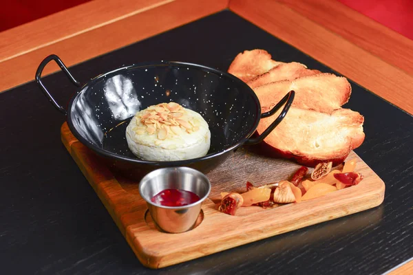 Baked Cheese - Melted cheese with bread and sauce served in a bowl on wooden rustic cutting board.