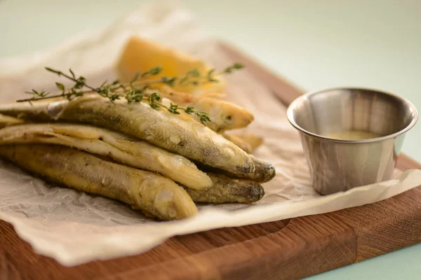 Smażone rybie smakołyki w cieście z cytryną i sosem na drewnianej tacy, deska do krojenia na jasnopastelowym zielonym tle mięty — Zdjęcie stockowe