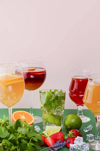 Five tropical mixed drinks, orange, lemon and raspberries cocktails over bright pastel green background.