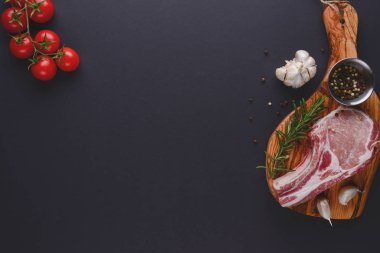 Taze çiğ biftek ahşap kesim tahtasında siyah arka planda baharatlarla, üst manzara.