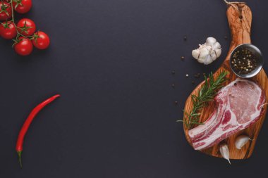 Taze çiğ biftek ahşap kesim tahtasında siyah arka planda baharatlarla, üst manzara.