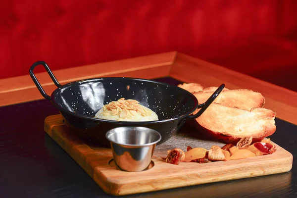 Baked Cheese - Melted cheese with bread and sauce served in a bowl on wooden rustic cutting board.