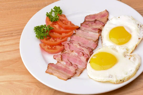 Petit déjeuner avec bacon, oeuf frit et tomates servi sur assiette blanche sur table en bois rustique léger . — Photo