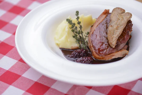 Aardappelpuree met vlees en jus geserveerd in een wit bord over rood geruit tafelkleed. — Stockfoto