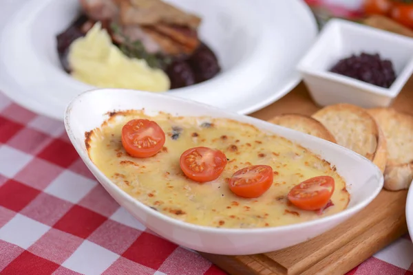 Italian lasagna close-up on the table. Served in a white bowl over red plaid tablecloth with other dishes. — Stock Photo, Image