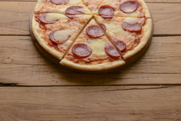 Flach lag Pfefferoni-Pizza isoliert auf rustikalem Holzboden. Pizzasalami in Scheiben geschnitten. Fast Food, Junk Food Konzept. — Stockfoto