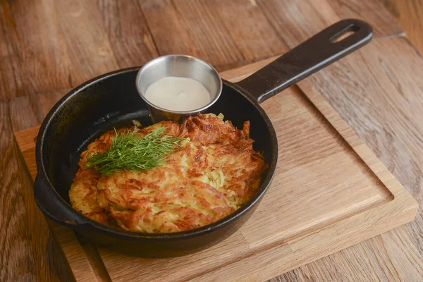 Köstliche Kartoffelpuffer mit Käse und Kräutern in einer Pfanne über hellem rustikalem Holzbrett. Abendessen im Restaurant. — Stockfoto