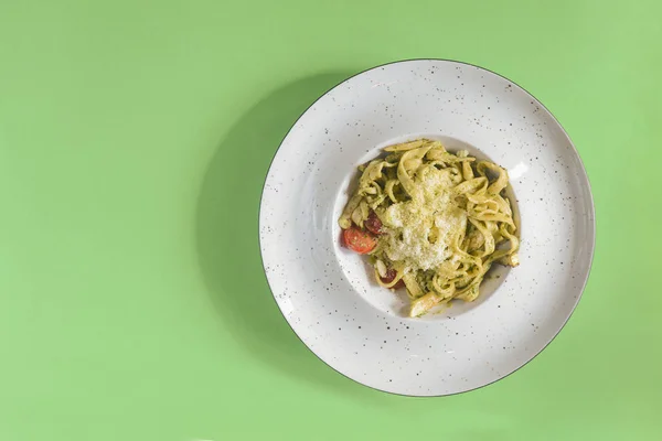 Délicieux plat végétarien de pâtes aux tomates et au persil servi dans une assiette blanche sur fond vert vif . — Photo