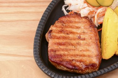 Izgara biftek, sebze ve domates sosu açık kırsal alanda siyah bir tabakta servis edilir..