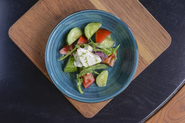 Um prato de salada de legumes com queijo feta, pepinos, tomates e brócolis servido em tigela em tábua de madeira rústica . — Fotografia de Stock