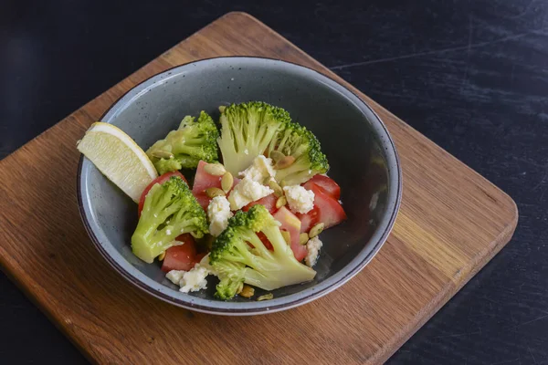 Um prato de salada de legumes com queijo feta, pepinos, tomates e brócolis servido em tigela em tábua de madeira rústica . — Fotografia de Stock