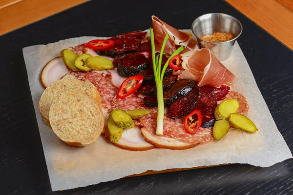 Meat carpaccio with greenery and vegetables on paper tray over dark rustic wooden table.