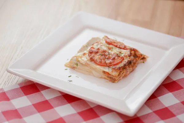 Malý kousek rajčatových lasagní na čtvercové bílé desce. Večeře v restauraci, kavárně nebo bistru. Koncept zdravé stravy. — Stock fotografie