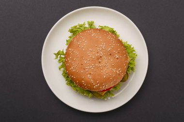 Siyah arka planda beyaz tabakta servis edilen klasik hamburger. Köfte düzdü. Abur cubur, fast food konsepti.