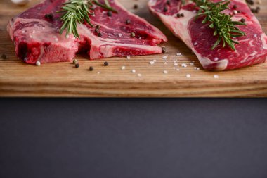 Ahşap kesme tahtasında taze çiğ biftek, siyah arka planda baharatlar, üst manzara..