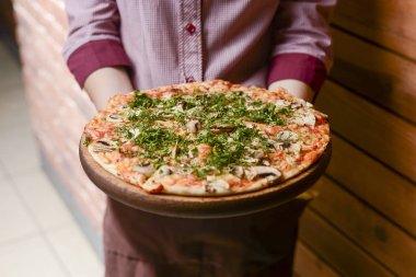 Bir garson lezzetli bir tabak yemek tutar. Restoranda İtalyan mutfağı, etli, zeytinli ve mantarlı lezzetli pizza..