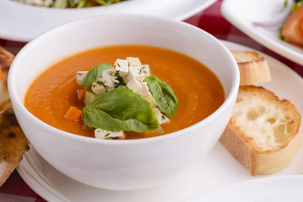 Pumpkin soup with feta cheese and vegetables served in white bowl topped with spinach with other Italian dishes — Stok fotoğraf