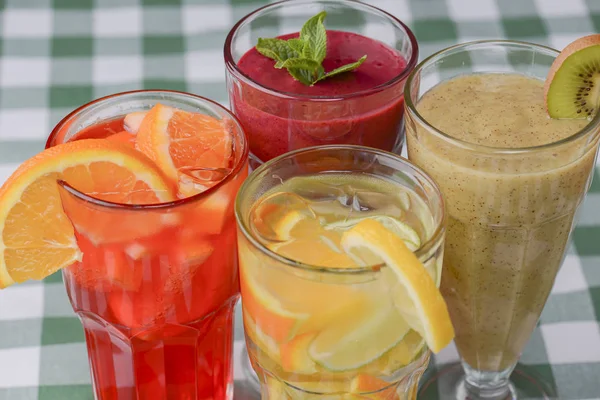 Four tropical mixed drinks, berries, orange and kiwi fruit cocktails served on green plaid tablecloth. — Stock Photo, Image