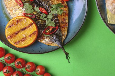 Taze otlu ve limonlu kızarmış balık, yeşil arka planda mavi bir tabakta servis ediliyor..