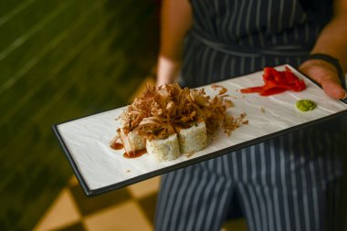 Üniformalı garson bir restoranda suşi rulosu tabağı tutuyor. Yemek fotoğrafçılığı konsepti. Japon mutfağı..