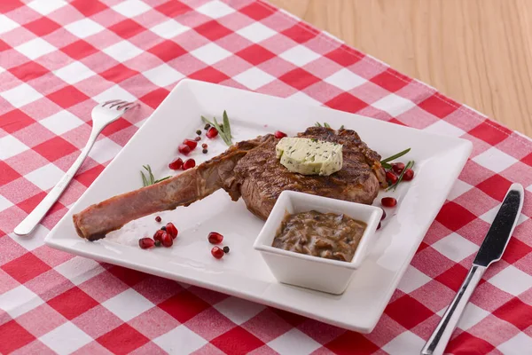 Estante de cordero servido con semillas de granada y salsa en un plato blanco sobre mantel a cuadros rojo. Concepto italiano . — Foto de Stock