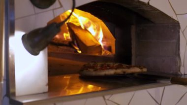 İtalyan pizzası Pepperoni fırında pişiriliyor, restoran şefi restorandaki ahşap fırından pizza çıkarıyor..