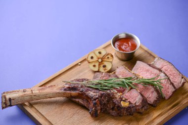 Dilimlenmiş ızgara az pişmiş ızgara biftek kemiğin üzerinde baharatlı ahşap bir tahtada servis edilmiş mavi arka planda..