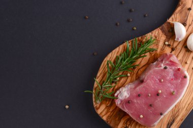 Taze çiğ biftek ahşap kesim tahtasında siyah arka planda baharatlarla, üst manzara.