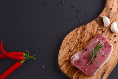 Taze çiğ biftek ahşap kesim tahtasında siyah arka planda baharatlarla, üst manzara.