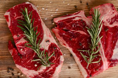 Taze çiğ biftek ahşap kesim tahtasında siyah arka planda baharatlarla, üst manzara.