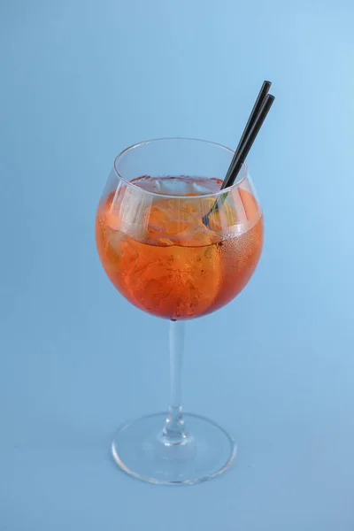 Холодный летний алкогольный коктейль со льдом и апельсином в бокале вина и черная пластиковая солома на светло-пастельно-голубом фоне — стоковое фото