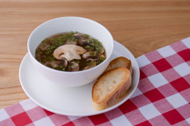 Kırmızı ekose masa örtüsüyle beyaz bir kasede servis edilen sebzeli tavuk çorbası ve et..