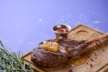 Izgara az pişmiş ızgara ızgara biftek ve ahşap bir tahtada servis edilen baharatlar ve mavi arka planda sos..