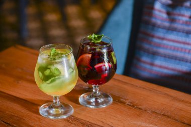 Two colorful refreshing cocktails served on a dark rustic wooden table with blurred background.