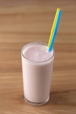 Vanilyalı çilekli milkshake, açık sade ahşap masa üzerinde iki plastik kamışla uzun bir galede..