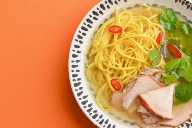 Miso ramen Asya eriştesi, taze yeşillik, parlak turuncu arka planda izole edilmiş bir kasede..