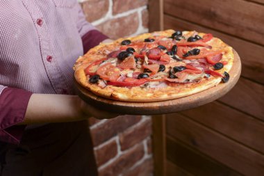 Farklı peynirli, domatesli, siyah zeytinli lezzetli pizza. Garson bir tabak lezzetli yemek hazırlıyor..