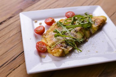 Kare beyaz tabakta servis edilen sebzeli omlet koyu kırsal ahşap masa arka planında..