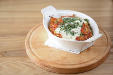 Beyaz kasede servis edilen ev yapımı et lazanyası, ahşap arka planda..