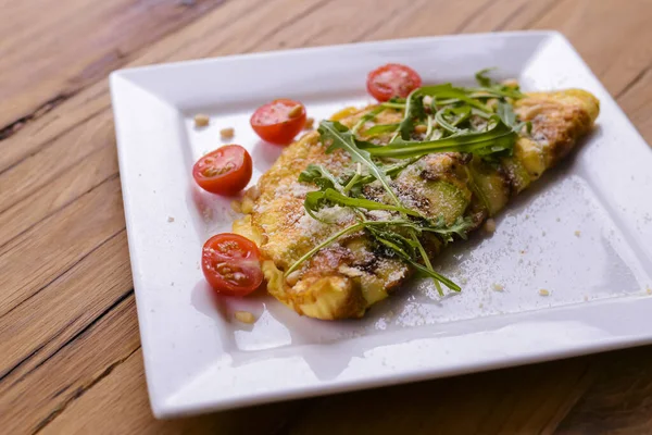Kare beyaz tabakta servis edilen sebzeli omlet koyu kırsal ahşap masa arka planında..