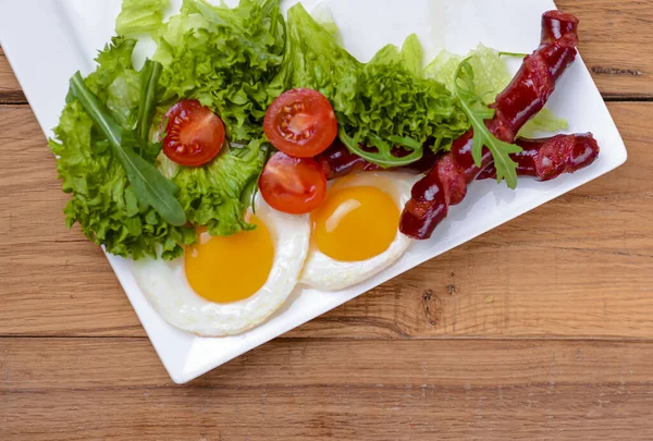 Śniadanie z bekonem, jajkiem smażonym i pomidorami na białym talerzu nad jasnorustykalnym drewnianym stołem. — Zdjęcie stockowe