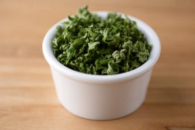 Köy ahşap masasının üzerinde lezzetli taze yeşilliklerle dolu bir kase. Bir kasede yeşil soğan.